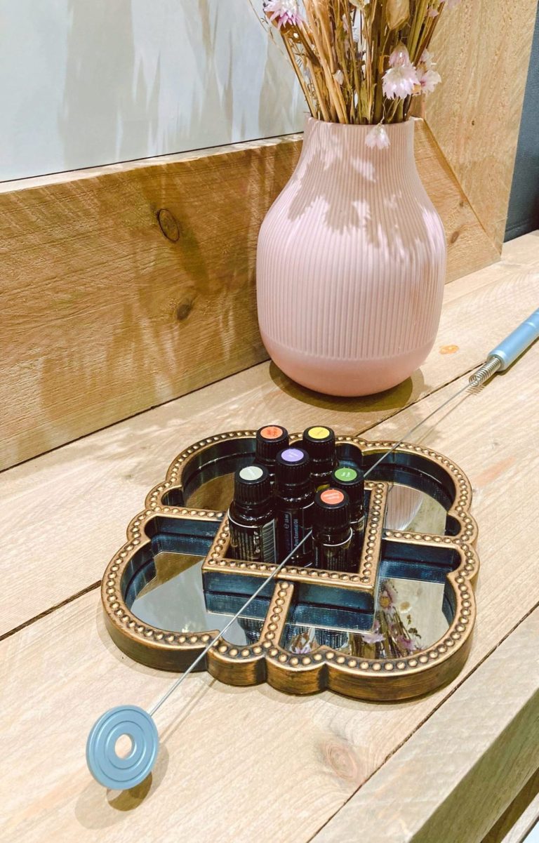 Een houten dienblad met kleurrijke kaarsen en een roze vaas op een houten tafel.