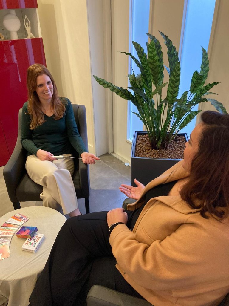 Twee vrouwen zitten in meubels en hebben een gesprek in een lichte ruimte.